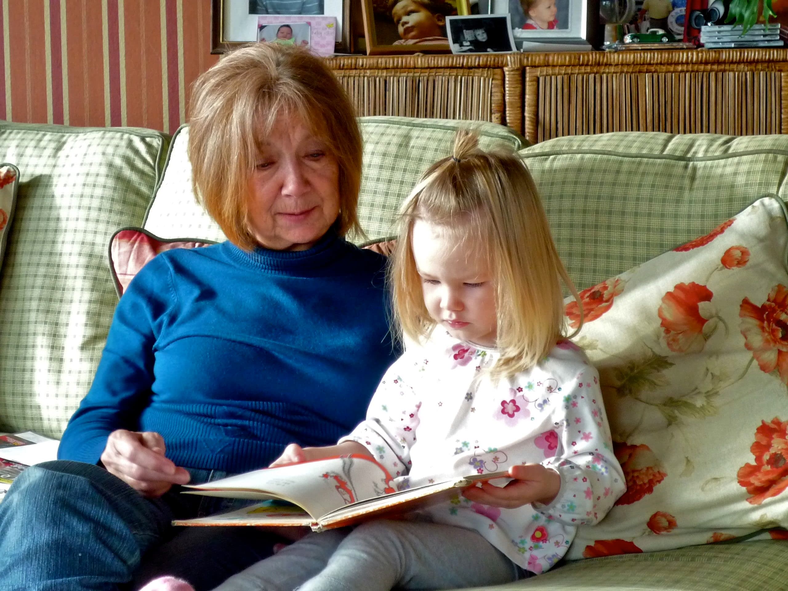 Wanda sitting on a sofa reading a picture book with a small girl leaning against her