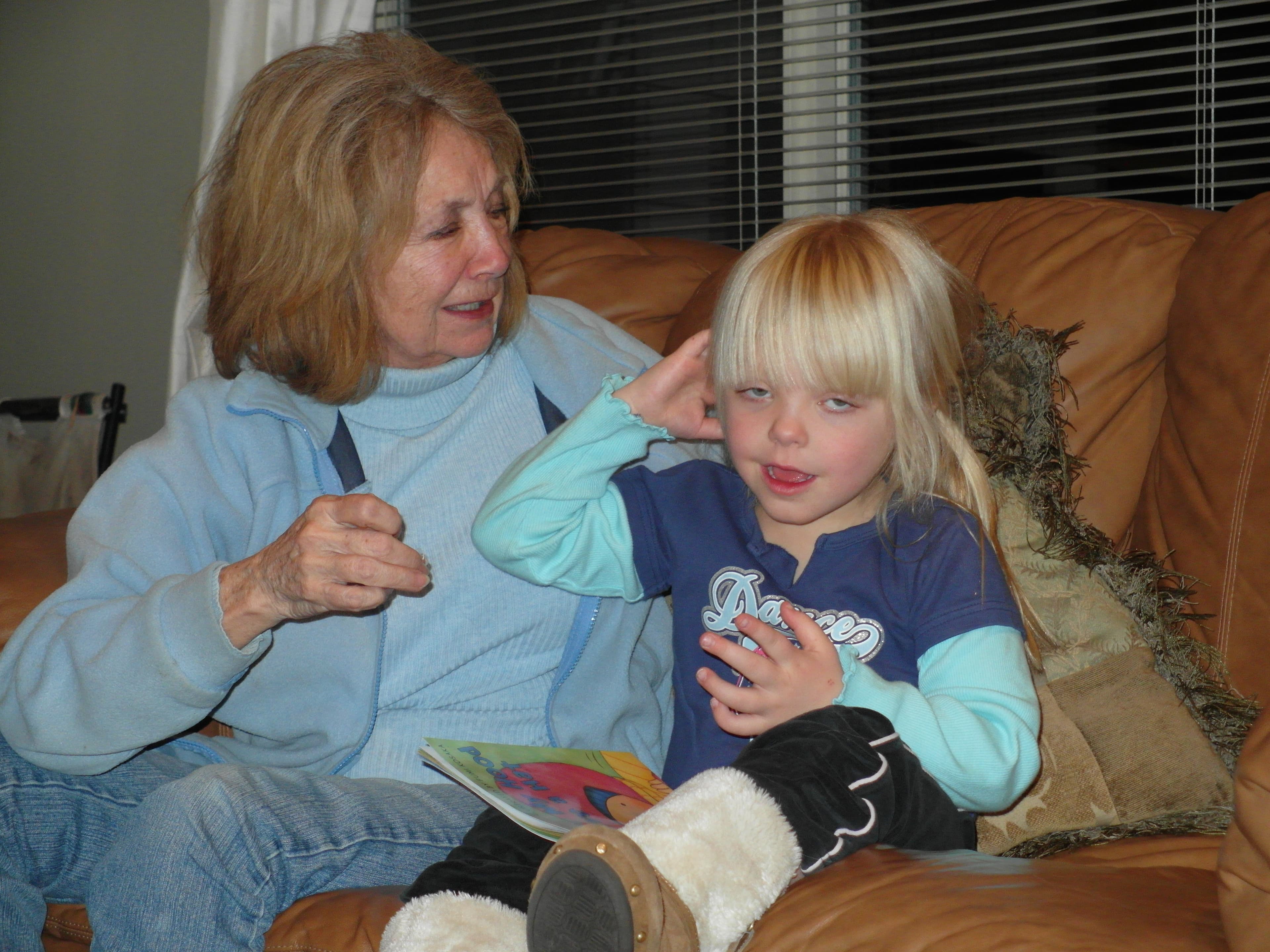 Wanda on a sofa mid-sentence with a young girl beside her, an open book on her lap